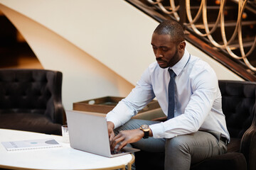 Portrait of African-American businessman using laptop while working in hotel lounge, copy space