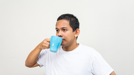 A portrait of Asian Malay man sipping a drinks from blue tea cup on his hand. Stay hydrate. Looking away with serious pensive expression, making plans for day. People and lifestyle