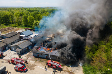 Aerial view of firefighters extinguishing ruined building on fire with collapsed roof and rising dark smoke.