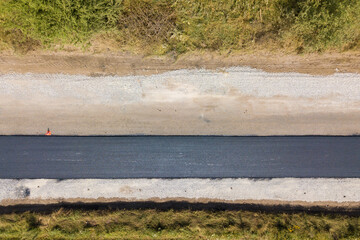 Aerial view of new road construction with newly layed black asphalt lane.