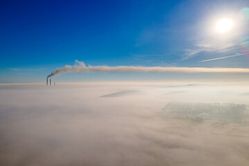 Aerial view of winter landscape with foggy countryside and distant factory pipes emmiting black dirty smoke polluting environment.
