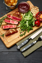 Grilled sliced roated beef steaks, potato and sauce on wooden cutting board