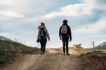 Young couple with backpacks and a dog walking in the mountains. Man and woman warmly dressed on hiking path.