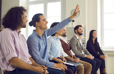 Young man in the audience raises his hand to ask a question. Group of happy people listening to a...