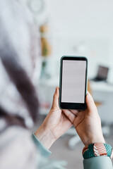 Vertical close up of ethnic young woman holding smartphone in office focus on blank white screen, copy space