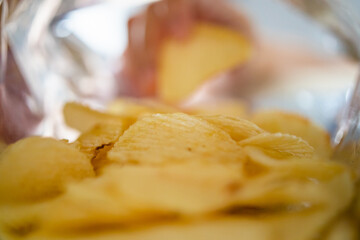 Hand picking potato chips inside snack bag