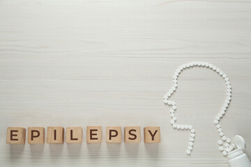 Wooden cubes with word Epilepsy and human head silhouette made of pills on white table, flat lay....