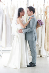 Naklejka premium The groom and the bride are standing, smiling and hugging in background of a bride's dress. A woman holding a purple bouquet Represents love for man. Concept wedding best day.