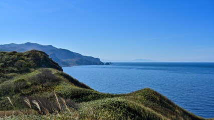 Fototapeta na wymiar 神威岬展望台から見た霞む山並みと積丹ブルーに染まる日本海の情景＠積丹、北海道