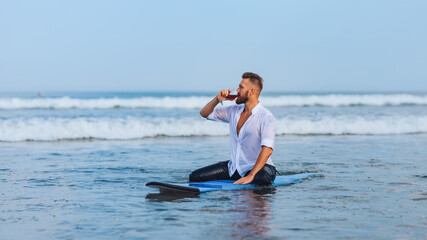 .European man drinking wine while sitting on a surfboard.