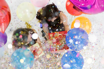 Two young and beautiful sexy Asian girls with colorful gift box dancing and playing with fun and happiness in a party with the bright color balloon in the background. Taken from a top-down angle.