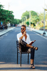 The guy sits on a chair on the roadway.