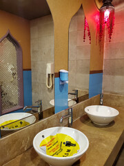 Orient style bathroom interior with Arabic shaped mirrors. Social distancing yellow sign inside sink forbidding to use it due to covid restriction