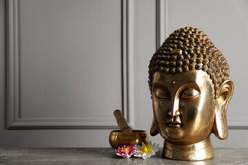 Buddha statue, singing bowl and lotus flowers on grey table. Space for text