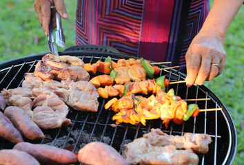 Closeup of  grilled chicken barbecue , pork and tomato on gridiron with elderly woman's hands.