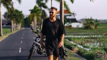 A young guy in dark clothes and glasses walks along the road.