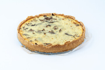 Studio shot of freshly baked yellow French salty cake, or quiche, with mushrooms, on a baking paper, isolated on white background.