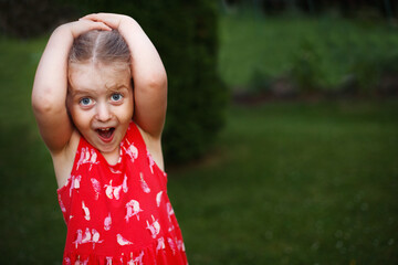 Portrait of a happy surprised cute little girl in a field in the red dress on green grass background