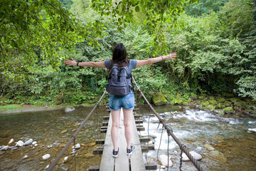 A slender brunette standing on a suspended bridge spread her arms to the sides.