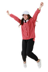 Delighted ethnic female in cool outfit and with headphones on neck in moment of jumping on white background in studio