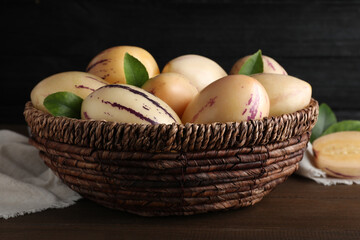 Fresh ripe pepino melons with green leaves in wicker basket on wooden table