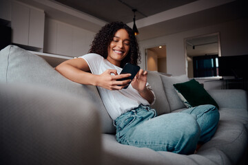 Mixed race female smiling while relaxing on couch typing on cellular device High quality 4k footage