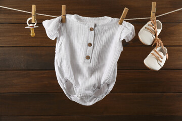 Baby clothes and accessories hanging on washing line near wooden wall