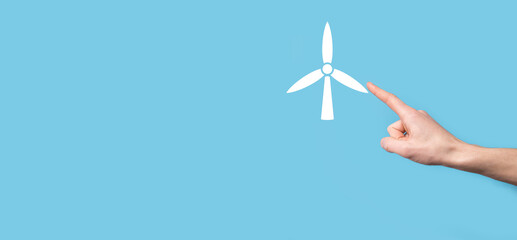 Hand holding an icon of a windmill that produces environmental energy on blue background.