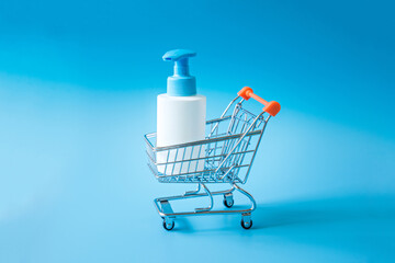 White plastic bottle with dispenser in a miniature supermarket trolley on a light blue background.