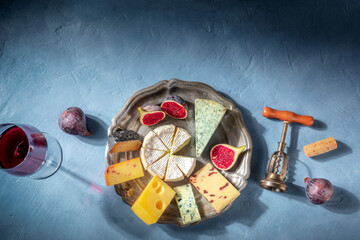 Cheese assortment with wine and fruit, a romantic French dinner, shot from above on a blue background with a place for text