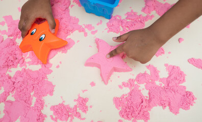 There is a child's hand on a background of pink science sand and bright plastic toys.