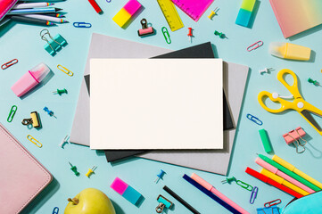Creative student desk with white sheet of notebook paper and school supplies. Top view with copy space. Back to school flat lay on blue and pink background