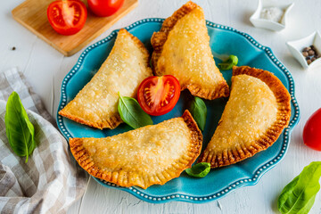 Chebureks or pasties, traditional deep-fried meat pies on a blue plate on a light concrete background.