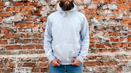 City portrait of handsome hipster guy with beard wearing gray blank hoodie or sweatshirt and hat with space for your logo or design. Mockup for print