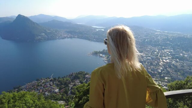 elegant woman on top of Lugano Swiss city by Lugano Lake in Switzerland. Aerial view lookout from Monte Bre Mount. Lugano cityscape with San Salvatore mount in Ticino canton.