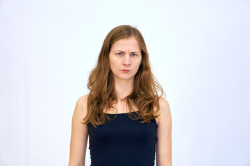 Serious emotion and frowning brows. beautiful Caucasian woman stands on a white background in a blue sweater with loose hair. The woman shows emotions.