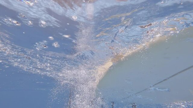 Woman surfer on surf board floats on water on hot sunny day, bottom view, underwater shot.