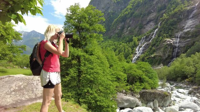 Woman photographer taking pictures at the old Roman stone bridge Steinbrucke over the Bavona River. Looking at the waterfall of Bavona valley in Switzerland. Bavona river leading to Lake Langensee.