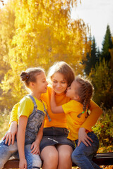 Fototapeta premium Two young little girl and his mother with blonde hair in an autumn park on a yellow and orange leaf background. Family walking in forest