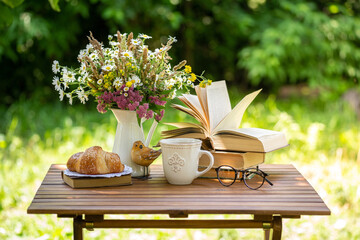 Bouquet of meadow flowers, croissant, cup of tea or coffee, books on table in summer idyllic...