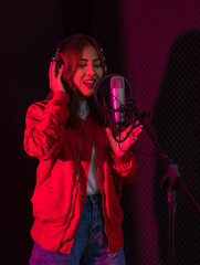 Ethnic female singer in headphones singing in microphone and recording music in studio