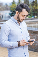 Obraz premium Portrait of a man businessman in a shirt with a beard who stands and uses a smartphone