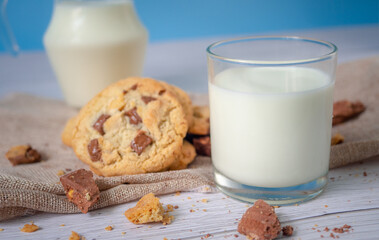 Delicious homemade chocolate chip cookies, paired with fresh milk in a glass and pitcher, placed on a white wooden floor and a blue background cloth. Drink in the morning for health and strong bones.