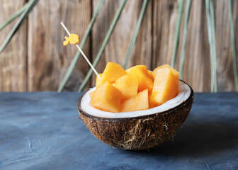Melon cut in cocco nut on the grey table with wooden background and palm branch