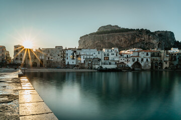 Fototapeta premium Sunrise in harbor of Cefalu, Sicily, Italy, old town panoramic view with colorful waterfront houses, sea and La Rocca cliff.Attractive summer cityscape,traveling concept background.Italian vacation.