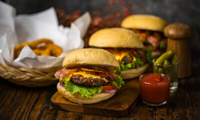 Selective focus on hamburgers with beef burgers, fried onions, spinach, ketchup, pepper and cheese served side dishes on a wooden board with soft drink.