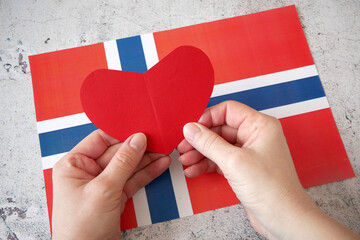 I love Norway. Hands puts paper red heart on Norway flag background. Norway Constitution Day - 17 of May