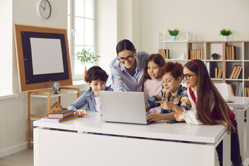 Computer science lesson. Elementary school kids and female teacher in school classroom working...