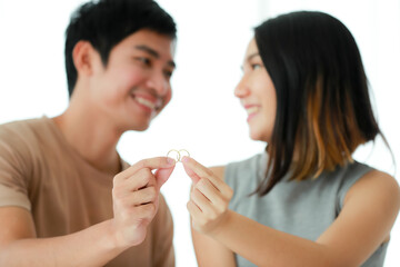Cute smiling young Asian lover couple in casual clothes, showing a golden engagement rings together. Love and marraigek concept.