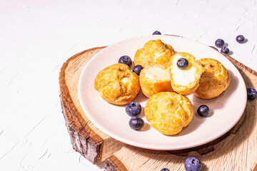 Profiteroles with blueberries. Custard cakes, Eclair, cream puff on a wooden stand
